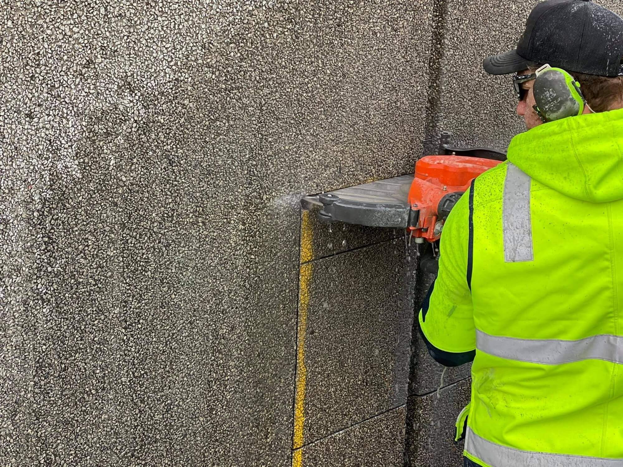 Operator running a handheld demolition saw through a concrete wall section