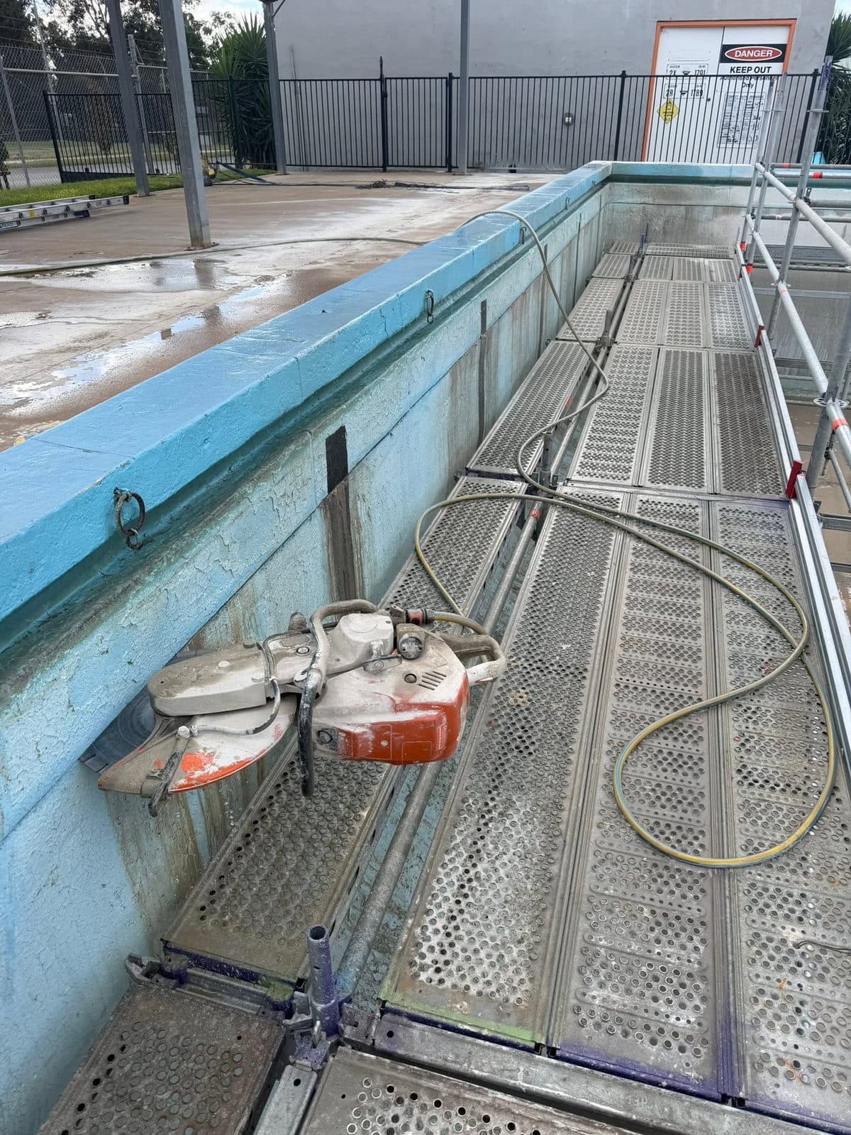 Hand saw and ring saw set up on planks over an empty pool shell ready to cut