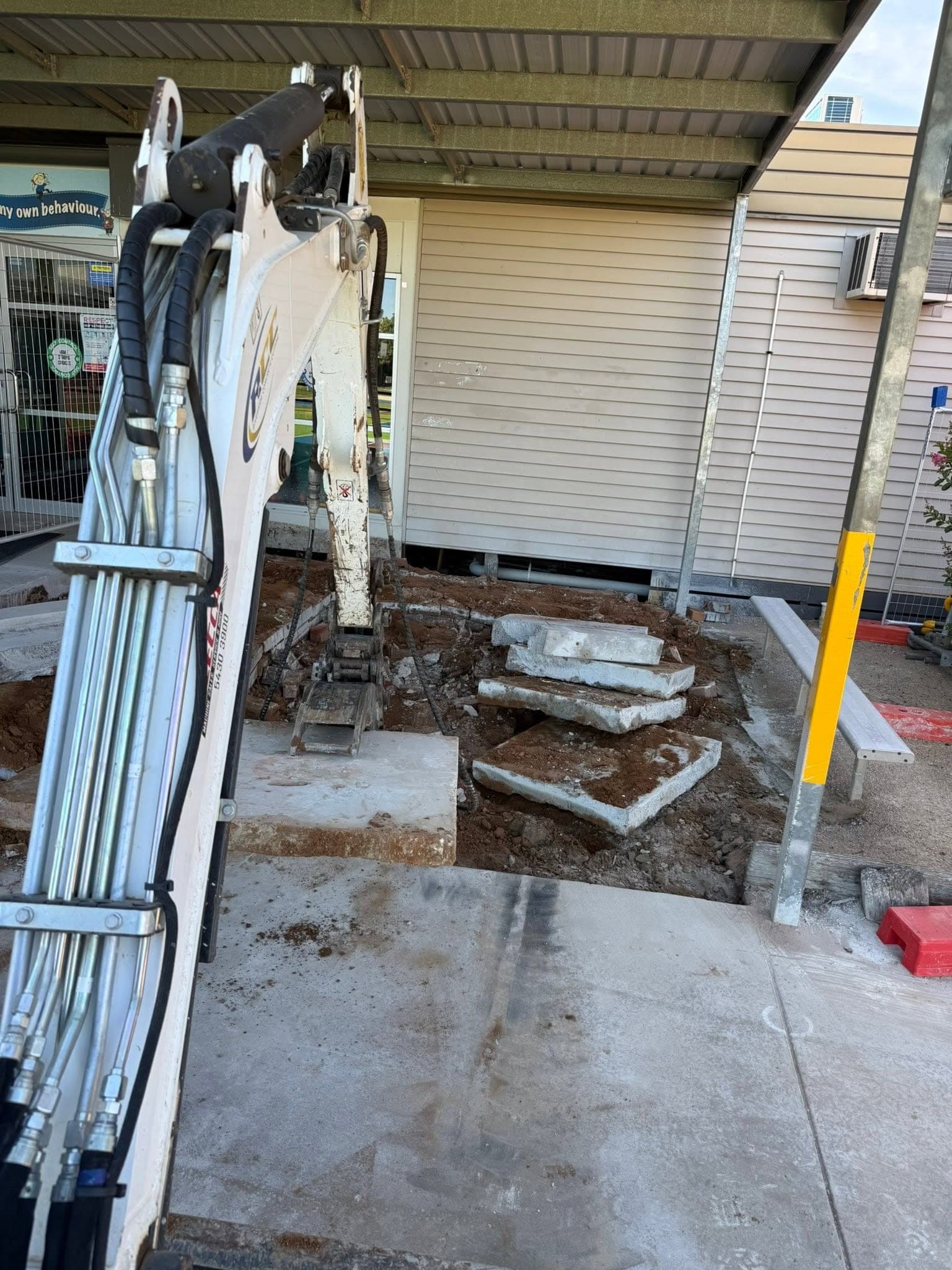 Excavator lifting saw cut slab sections clear of a floor for removal