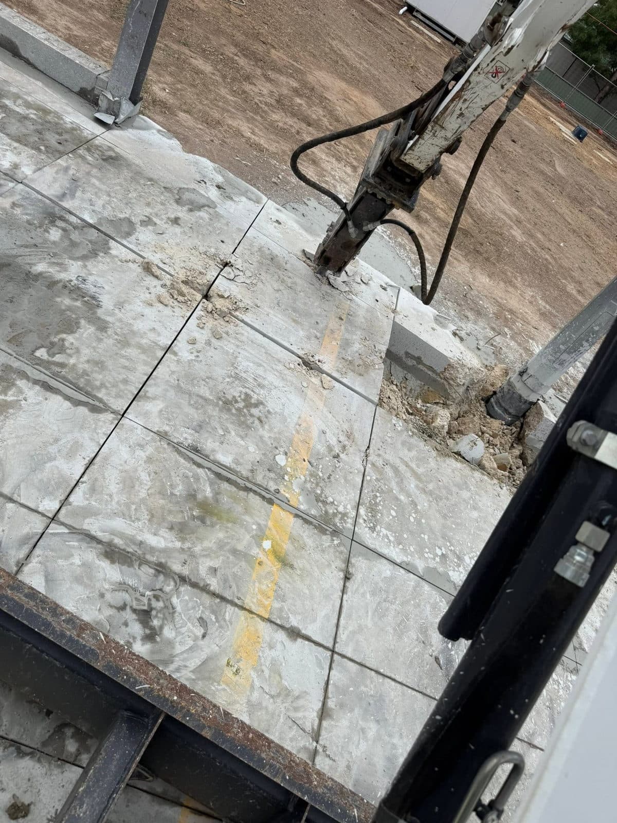 Excavator lifting a saw cut section of concrete slab out for removal