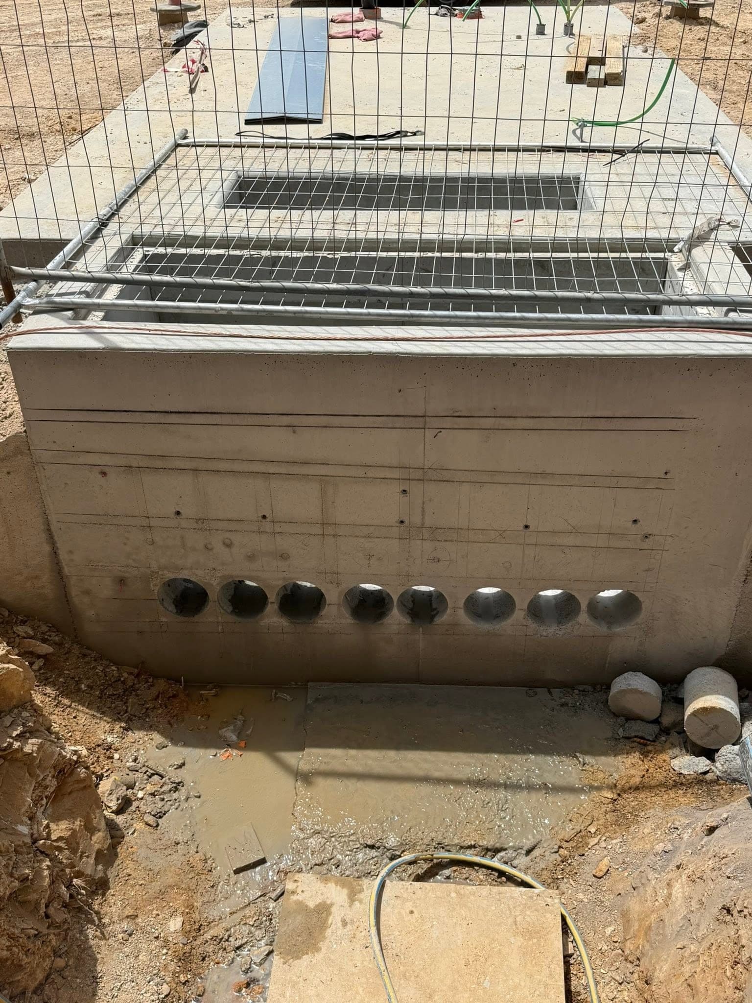Row of cored penetrations through a concrete pit wall with the cut cores stacked beside it